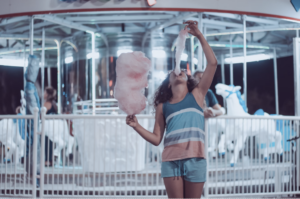 girl eating cotton candy in front of carousel